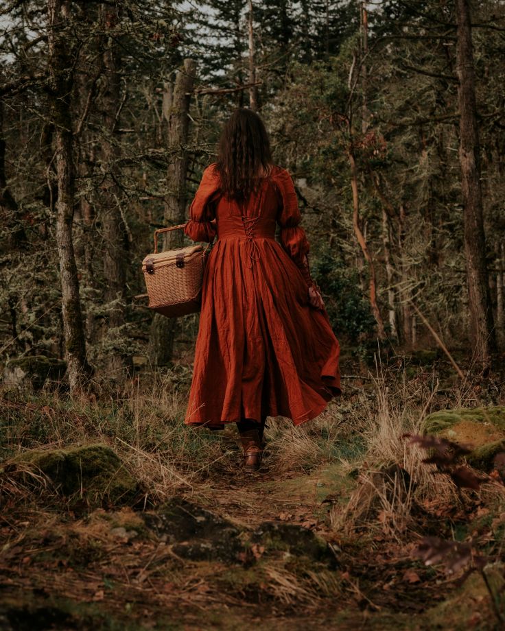 women in a red dress walking in a forest with a basket